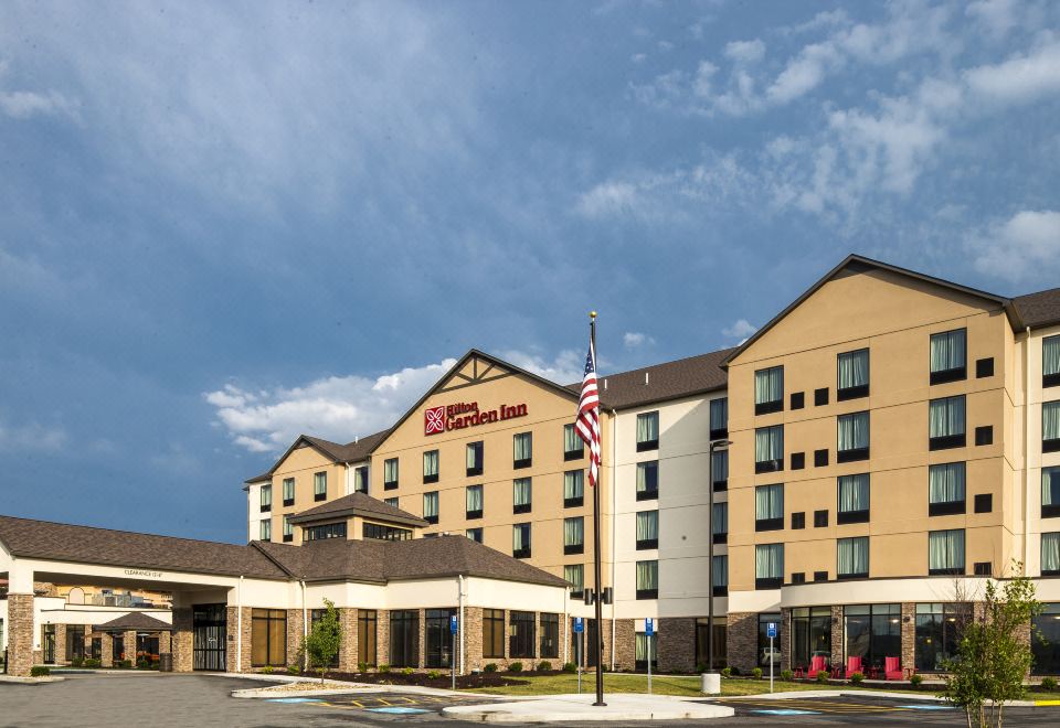 a large hotel with a flagpole in front of it and a clear blue sky behind it at Hilton Garden Inn Uniontown