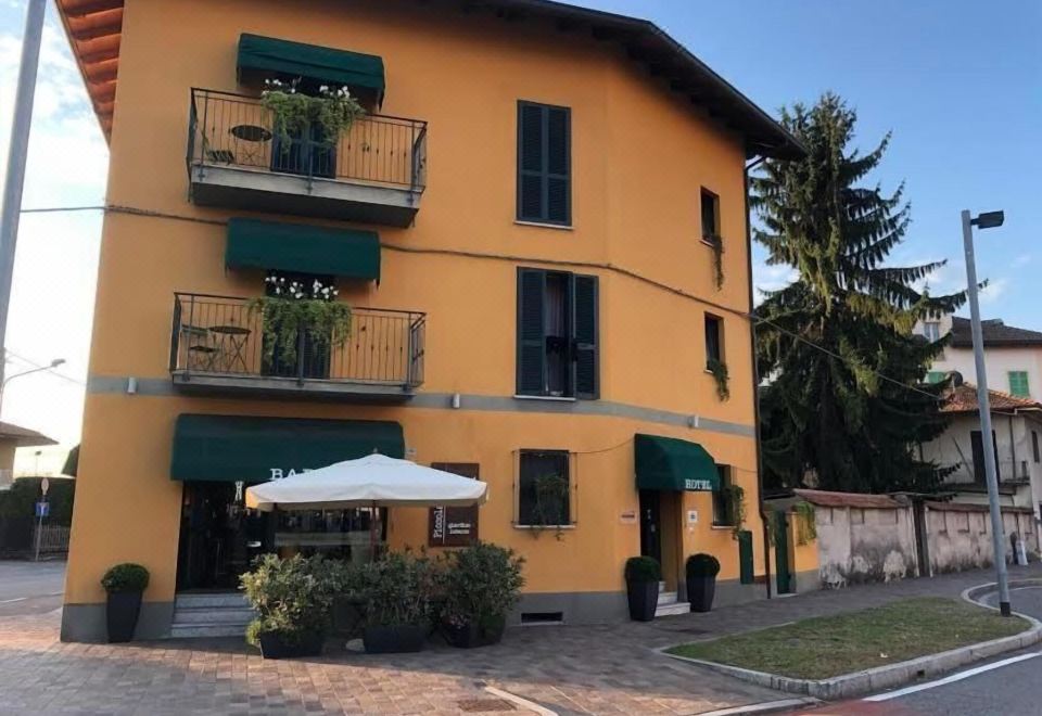 a yellow building with balconies and a white umbrella on the side , surrounded by trees at Hotel Del Corso