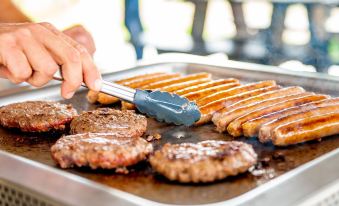 a person is cooking a variety of food items , including sausages and burgers , on a grill at Discovery Parks - Bunbury