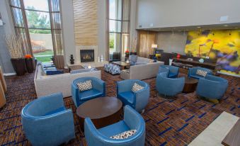 a modern living room with blue chairs and couches , a fireplace , and large windows overlooking the outdoors at Courtyard Boston Raynham