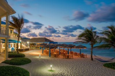 a beachside restaurant at dusk , with umbrellas and tables set up for patrons to enjoy their meal at Wyndham Reef Resort Grand Cayman