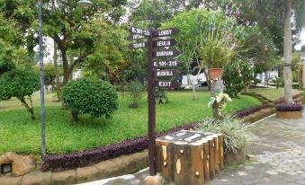 a park with a wooden sign pointing in different directions , surrounded by trees and grass at Front One Resort Magelang