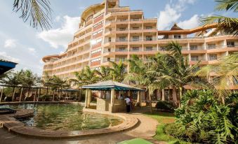 a large building with a pool and palm trees in front of it , under a blue sky at Rainbow Ruiru Resort