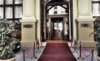 a red carpet leads to a building with columns and a large archway entrance decorated with gold ropes at Grand Hotel Et des Palmes