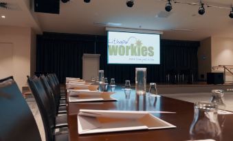 "a conference room with a large screen displaying "" always works "" and empty tables set up for an event" at Lithgow Workies Club Motel