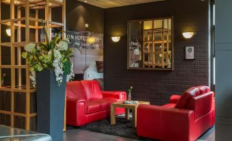 a cozy living room with red couches , a wooden coffee table , and a black couch , along with a vase of flowers on the coffee at Bastion Hotel Bussum Hilversum