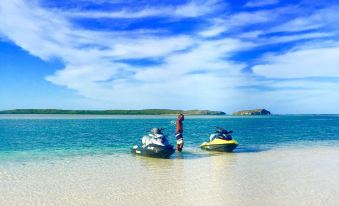 a man is standing on a beach next to two jet skis , enjoying the clear blue water at Pelican Beach Hotel