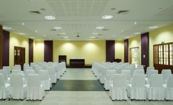 a large , empty conference room with rows of white chairs and purple columns , set up for an event at Poovar Island Resort