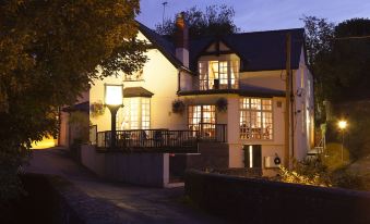 a large , two - story house with a balcony and windows is lit up at night , surrounded by trees at The Newbridge on Usk