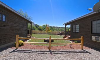 a gravel driveway leading to a wooden house surrounded by grass and trees , with a fence surrounding the property at The Escape to East Zion