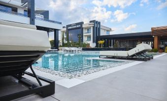 a large outdoor swimming pool surrounded by a hotel building , with lounge chairs and umbrellas placed around the pool at Hotel Mirror Skopje