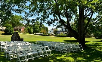 a lush green lawn with rows of white chairs set up for an outdoor event , likely a wedding or celebration at The Brandon Inn