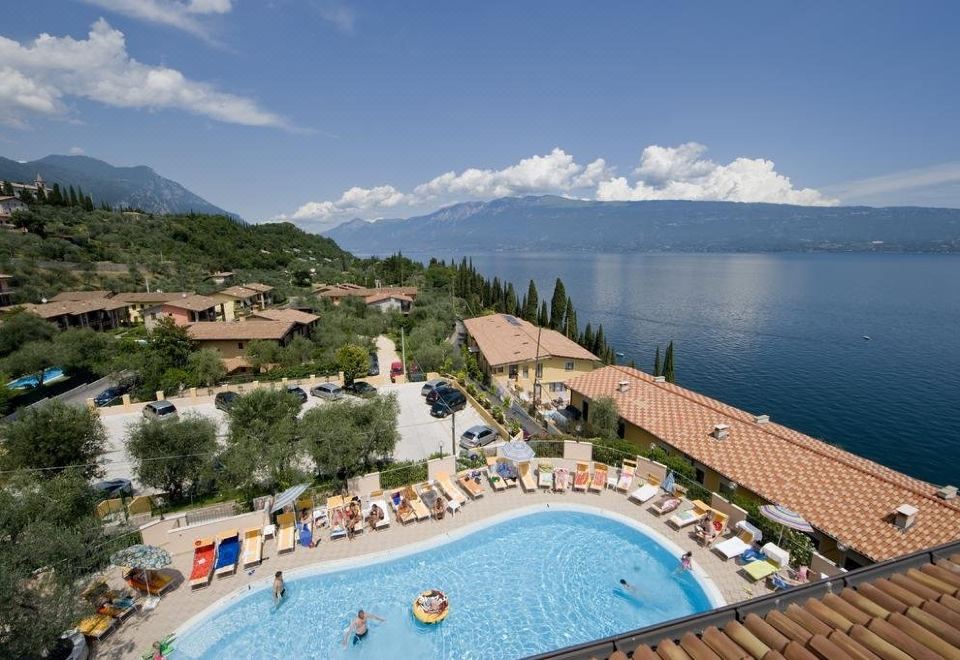 a resort with a large pool surrounded by lounge chairs and umbrellas , as well as a view of the lake and mountains in the background at All Inclusive Hotel Piccolo Paradiso