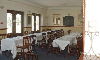 a large , empty dining room with white tablecloths and wooden chairs , set up for a formal dinner at Riverside Hotel