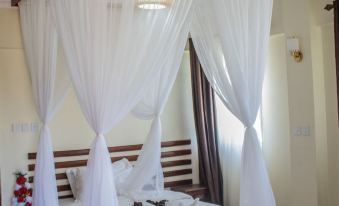 a bed with a canopy in a room , surrounded by white curtains and decorated with red flowers at Calabash Hotel