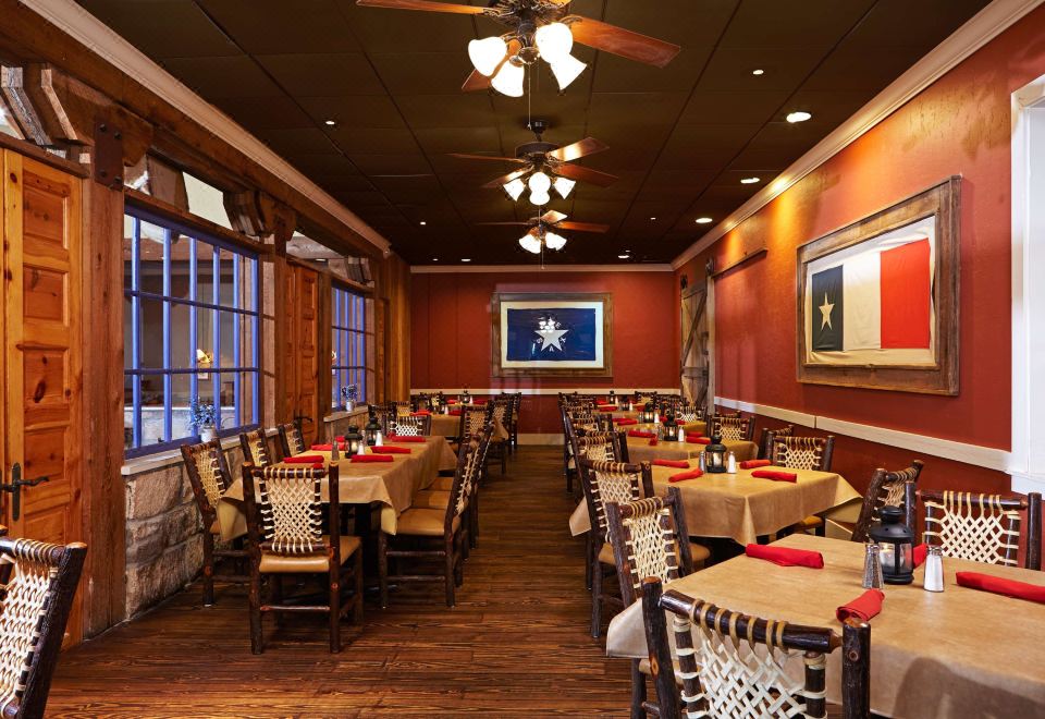 a large dining room with wooden tables and chairs , red walls , and a ceiling fan at Hilton Houston Westchase