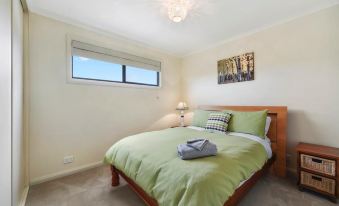 a cozy bedroom with a green bedspread , two pillows , and a window with a view of the outdoors at Seaspray