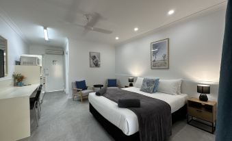 a modern hotel room with a large bed , white walls , and gray carpet , along with two beds and other amenities at Mareeba Motor Inn