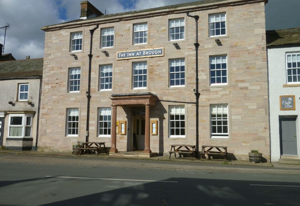 "a large stone building with a sign that says "" the inn at brackenrig "" and several benches in front" at The Inn at Brough