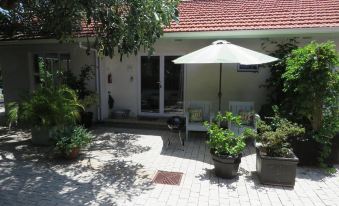 a backyard with a patio area , surrounded by potted plants and a white umbrella , under the shade of a tree at Bare Feet Retreat