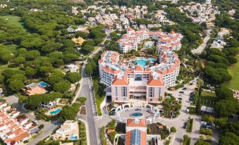 a large , multi - story building with a pool and multiple terraces is surrounded by trees and other buildings at Hilton Vilamoura As Cascatas Golf Resort & Spa