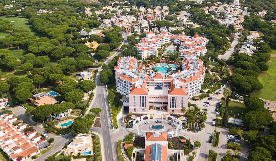 a large , multi - story building with a pool and multiple terraces is surrounded by trees and other buildings at Hilton Vilamoura As Cascatas Golf Resort & Spa