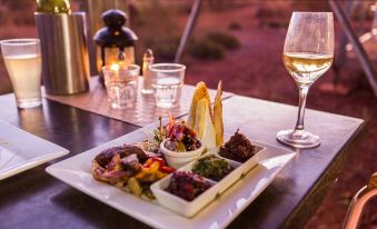 a dining table with a plate of food and a glass of wine , accompanied by a candle at Karijini Eco Retreat