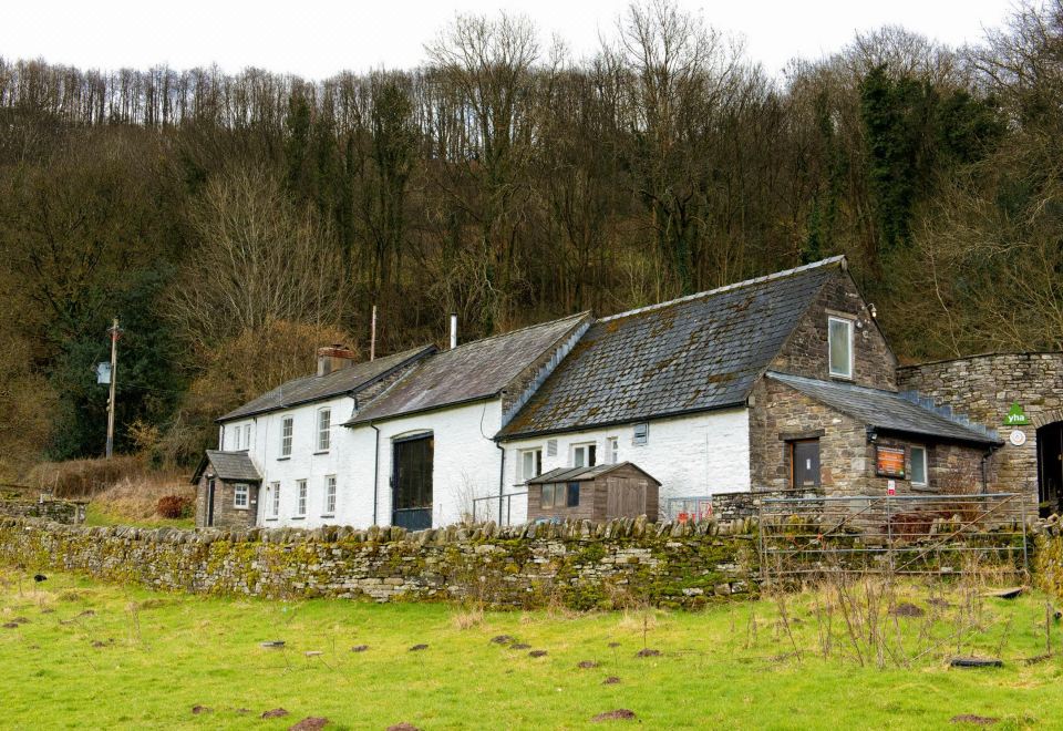 a rural landscape with a white barn surrounded by green grass and trees , located in the countryside at YHA Brecon Beacons Danywenallt