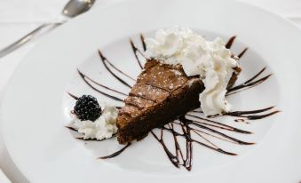 a slice of chocolate cake with whipped cream and a blackberry on a white plate at Hotel Motel Prestige