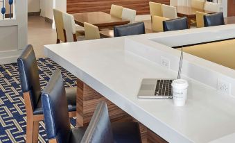 a modern hotel lobby with blue and white chairs , a long dining table , and a laptop on the desk at Sonesta ES Suites Cincinnati - Sharonville West