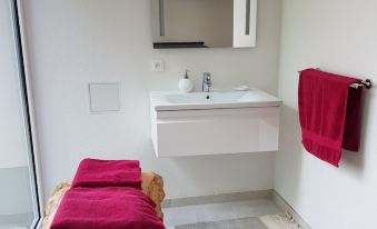 a modern bathroom with a white sink , red towels , and a wooden bench , along with a tv on the wall at La Roseraie