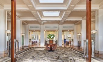 a large , well - lit hotel lobby with white columns and a carpeted floor , featuring a vase of flowers in the center at Hyatt Hotel Canberra - A Park Hyatt Hotel