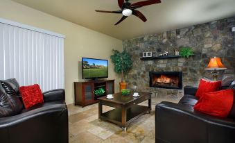 a living room with a fireplace , black leather couches , and a flat - screen tv mounted on the wall at Arrowhead