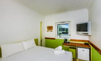 a clean and well - organized hotel room with a white bed , green wall , and a television at Ibis Budget Brisbane Airport