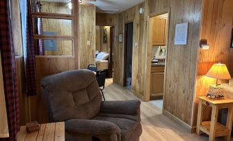 a living room with a brown recliner and wooden walls , leading to a kitchenette and bedroom at Hidden Haven Cottages