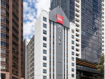 a tall hotel with a red sign on the top and other buildings in the background at Ibis Melbourne Hotel and Apartments