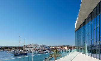 a modern building with a glass facade , situated next to a harbor with boats docked in the water at Tivoli Marina Vilamoura