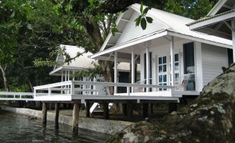 a white house with a dock in front of it , surrounded by trees and water at Driftwood Resort