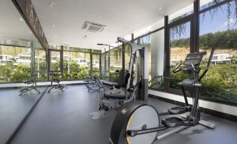 a well - equipped gym with various exercise equipment , including treadmills and weight machines , positioned near large windows that offer views of the outdoors at Ivory Villas & Resort