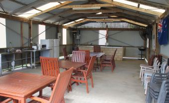 a wooden dining area with a table and chairs , surrounded by a barren structure under a large roof at Seaspray Beach Holiday Park