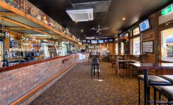 a bar with a brick wall , tv 's above the counter , and wooden tables and chairs at Prince of Wales Hotel Gulgong
