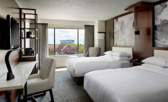 a modern hotel room with two beds , a window offering a view of the city , and white furniture at Marriott East Lansing at University Place