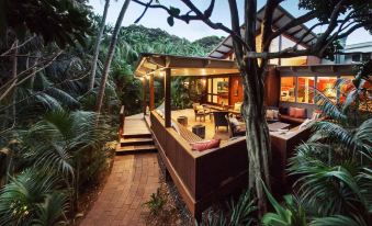 a modern , two - story house surrounded by lush greenery and trees , with a balcony and dining area at Arajilla Retreat
