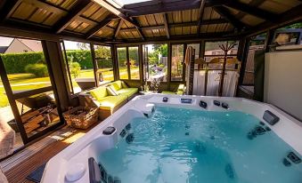 a large hot tub is situated in a room with a couch and chairs , surrounded by windows at Hôtel la Ramade