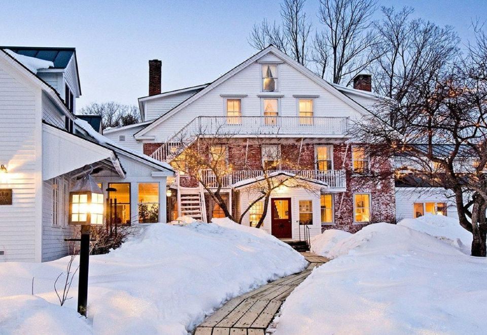 a snow - covered white house surrounded by snow - covered trees , with a staircase leading up to the entrance at Windham Hill Inn