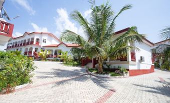 a white building with a red roof and palm trees in front of it , surrounded by a brick courtyard at Royal Elmount Hotel