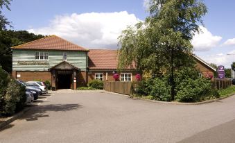 a brick building with a green roof and red brick walls , surrounded by trees and cars parked in the driveway at Premier Inn Dover East