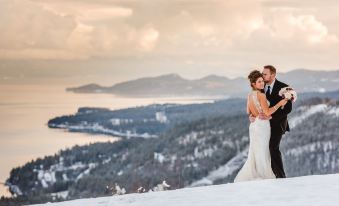 a bride and groom are standing on top of a snow - covered hill , embracing each other , with a scenic view of the mountains in the at Coyote Bluff Estate