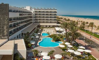 a large hotel with a pool surrounded by palm trees and umbrellas , located near the beach at RH Bayren Hotel & Spa