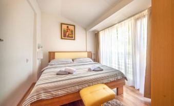 a bed with a striped blanket and yellow stool in a room with white walls at Tina